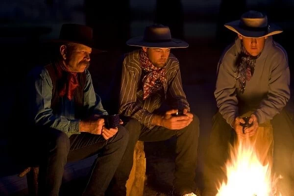 USA, Oregon, Seneca, Ponderosa Ranch. Three pensive cowboys hold mugs and watch an evening campfire
