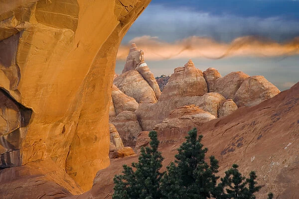 USA, Utah, Arches National Park. Setting sun illumines Skyline Arch, boulders, and spiral cloud