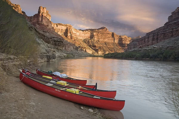 USA, Utah, Canyonlands National Park. Three red canoes rest on bank of Green River
