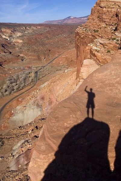USA, Utah, Capitol Reef National Park. The shadow of a hiker standing on cliffs above the highway