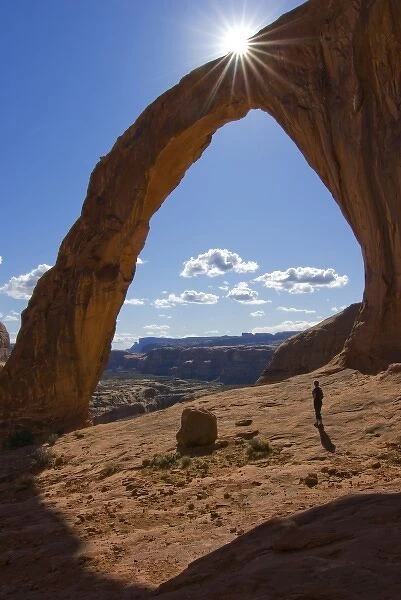 USA, Utah. A female hiker dwarfed by the Corona Arch near Moab. (MR)