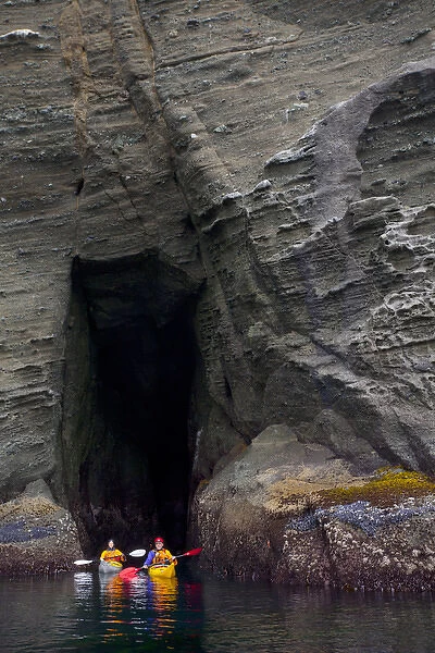 USA. Washington state. Man and woman sea kayakers explore a sea cave at Cape Flattery