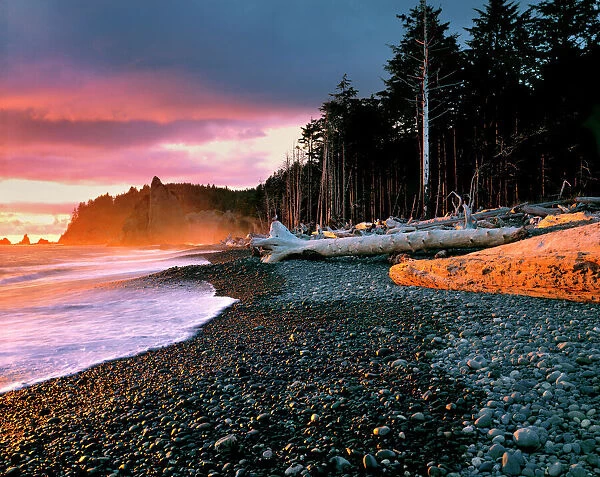 USA, Washington State, Olympic NP. Waves lap the rocky beach at sunset at Rialto Beach