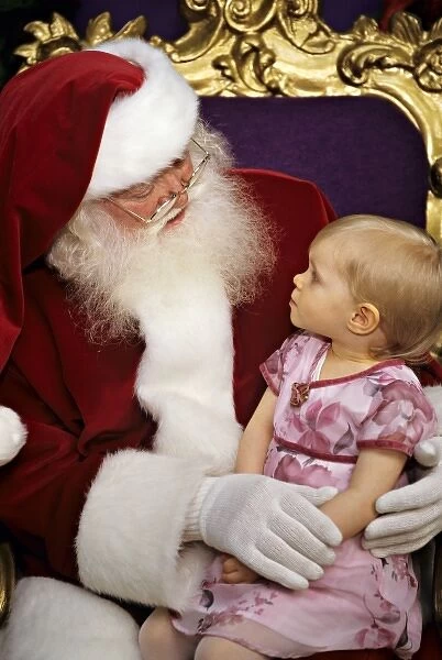 USA. Two year old girl sits on Santa Claus lap (MR)