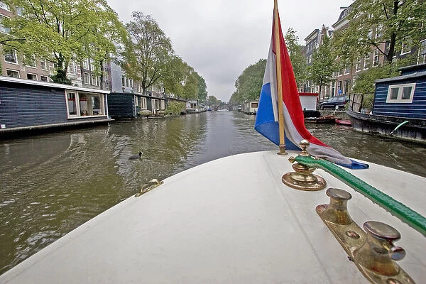 View from the front of a boat with a colorful flag, traveling a canal lined with