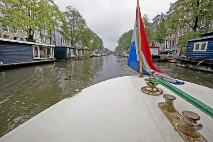 Framed Print : View from the front of a boat with a colorful flag, traveling a canal lined with