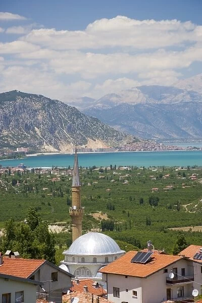 View of Lake Egirdir beyond hilly green land, village mosque with tin dome in front