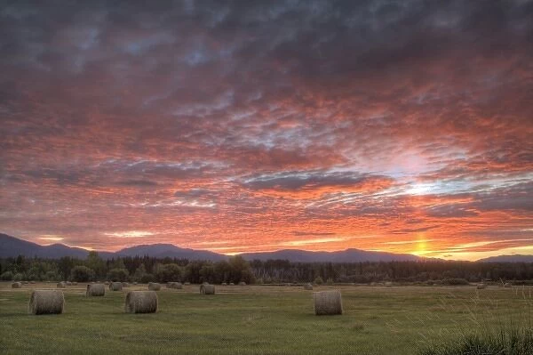 Vivid sunrise clouds over hay bales in field and the Whitefish Mountain Range in Montana
