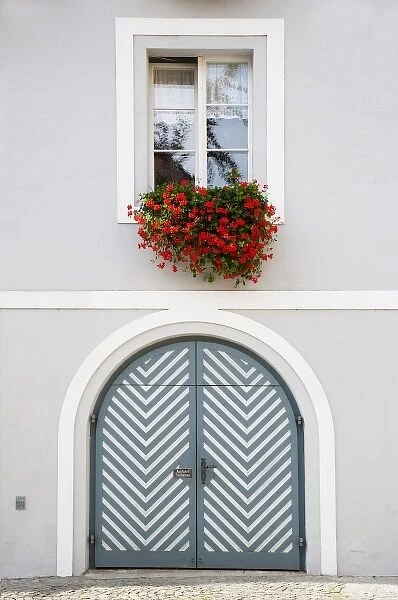 Wels, Upper Austria, Austria - Red flowers are hanging from an open window over a