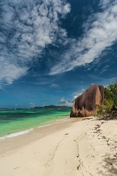 Wispy clouds over a sandy tropical beach with a large stone rock formation. Anse Source d Argent Beach, La Digue Island, Seychelles