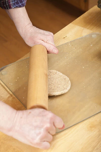 Woman rolling multigrain bread dough into circles to make hamburger buns. (MR)