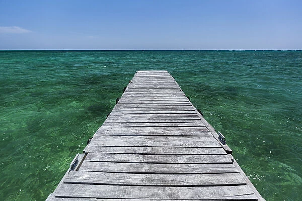 A wood dock in the foreground with clear green water and blue skies near the Isle of Youth