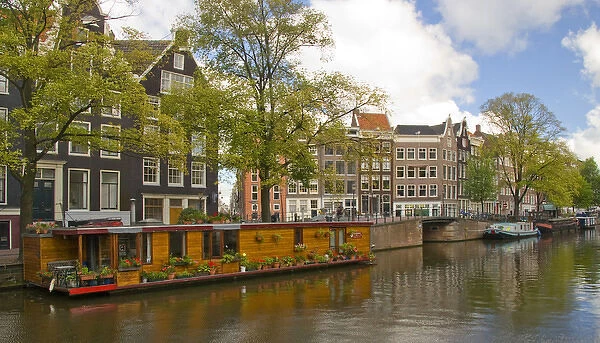 A wooden houseboat with lots of flowers on Prinsengracht Canal with colorful buildings