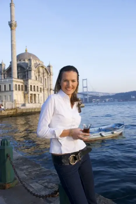 Framed Print : Young woman holding Turkish tea glass, in front of Great Mecidiye Mosque, Ortakoy on the Bosphorus