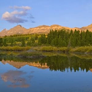 Beaver pond reflects first light on mountain peaks at Marias Pass in Glacier National