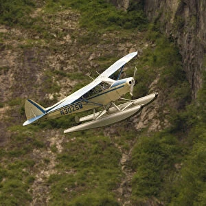A bush pilot flies his float plane close to mountain in Alaskan canyon