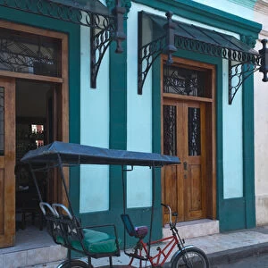 Camaquey Cuba street scene of old bike carriage on street and buildings