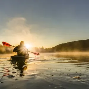 Canada, British Columbia. A kayaker paddles in sunlit early morning mist on a Canadian Canada, British Columbia. A kayaker paddles in sunlit early morning mist on a Canadian