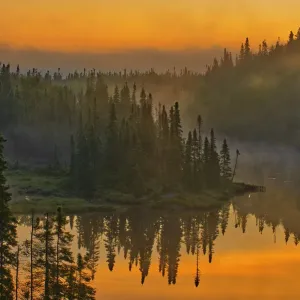 Canada, Ontario, Schreiber. Sunrise fog and forest reflect in lake