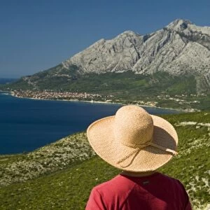 Croatia, Dalmatia, Female tourist in straw hat gazes at lush fields and town of Orebic