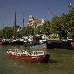Europe, Netherlands, Dordrecht. Boats lining canal, with tourist boat motoring by