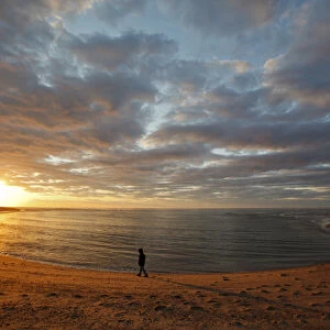 A girl walks on the beach a the sun sets over Head of the Meadow Beach at the Cape