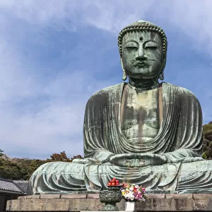 The Great Buddha, Daibutsu, offerings in front, blue sky above in Kamakura, Japan