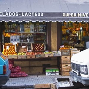 A grocery store with froits and vegetables displayed on the pavement. Cars parked in front