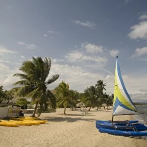 Hobiecat sailboat and kayaks on beach with palm trees by Caribbean Sea, Jaguar Reef Lodge