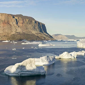 Iceberg in the Uummannaq Fjord System. Red cliffs of Storoen Island in the background