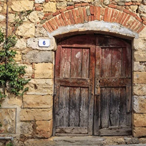 Italy, Monteriggioni. Stone wall, wooden door with planted geraniums