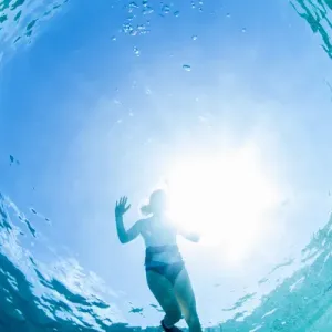 Looking up at a woman snorkeling in clear blue water near Staniel Cay, Exuma, Bahamas
