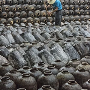 Man in the middle of big pile of wine jars stacked up at a local rice winery, Wuxi