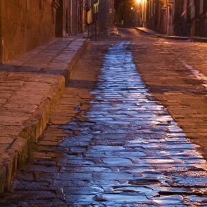 Mexico, San Miguel de Allende. Lanterns reflect on pre-dawn cobblestone street. Credit as