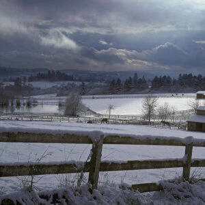 Shaft of light hits the snow-covered rural pasture with horses and barns near Lake Oswego