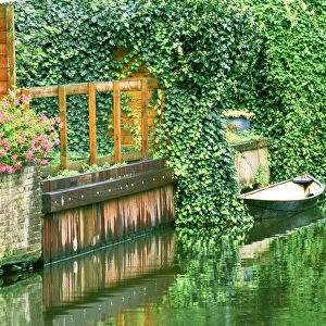 Small boat tied up in a canal next to a garden in Amsterdam