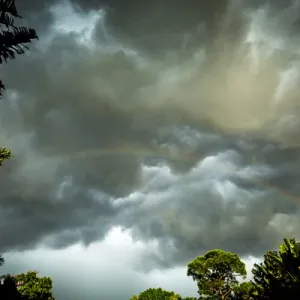 Storm clouds approach in this photograph while a rainbow is illuminated by sunrays