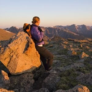 USA, Colorado, Rocky Mountain NP. A female hiker leans against a boulder on teh Longs Peak trail