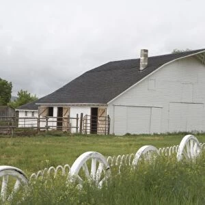USA, Idaho, Idaho Falls. White barn and wagon-wheel fence on farm. Credit as: Dennis