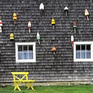 USA, Maine, Boothbay Harbor. Bright buoys decorate the weathered shingles of this