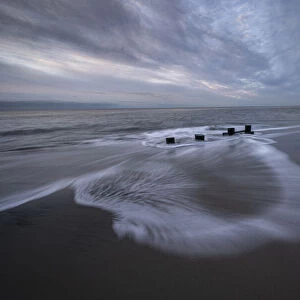 USA, New Jersey, Cape May National Seashore. Pier stumps on cloudy seashore sunrise