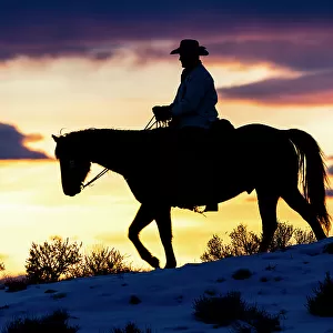 USA, Shell, Wyoming. Hideout Ranch cowboy on horseback silhouetted at sunset. (PR, MR)