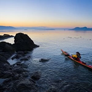 USA, Washington State, San Juan Islands, Doe Island. Woman sea kayaker paddling at dawn