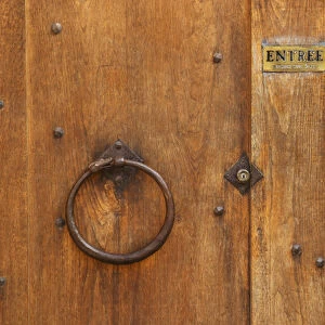 The wooden entrance door with metal ring knocker and old lock, sign saying entree, step in