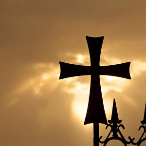 A wrought-iron cross on a fence in Syria at sunrise