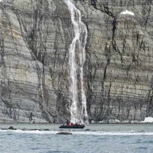 Zodiac approaching waterfall and king penguins on the beach, Gold Harbour, South Georgia