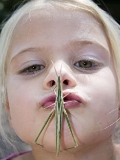 Africa, Kenya. Young girl puckers up with grasshopper on her mouth. (MR)