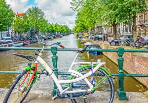 Bicycle Prints: Amsterdam, Netherlands. Wide angle view of brightly painted bicycle locked to a bridge crossing the canal