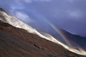 Asia, India, Ladakh, Zanskar Valley. A rainbow curves over the steep, stark mountain