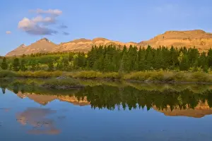 Beaver pond reflects first light on mountain peaks at Marias Pass in Glacier National